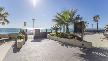 Un espace extérieur ensoleillé avec vue sur la mer, comprenant un coin salon agrémenté de jardinières et d’une structure en bois.