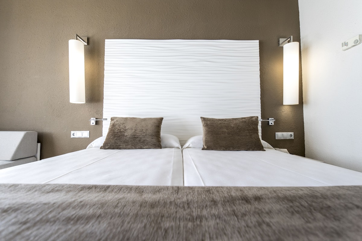 Un lit double avec une tête de lit texturée, deux appliques murales et deux oreillers.