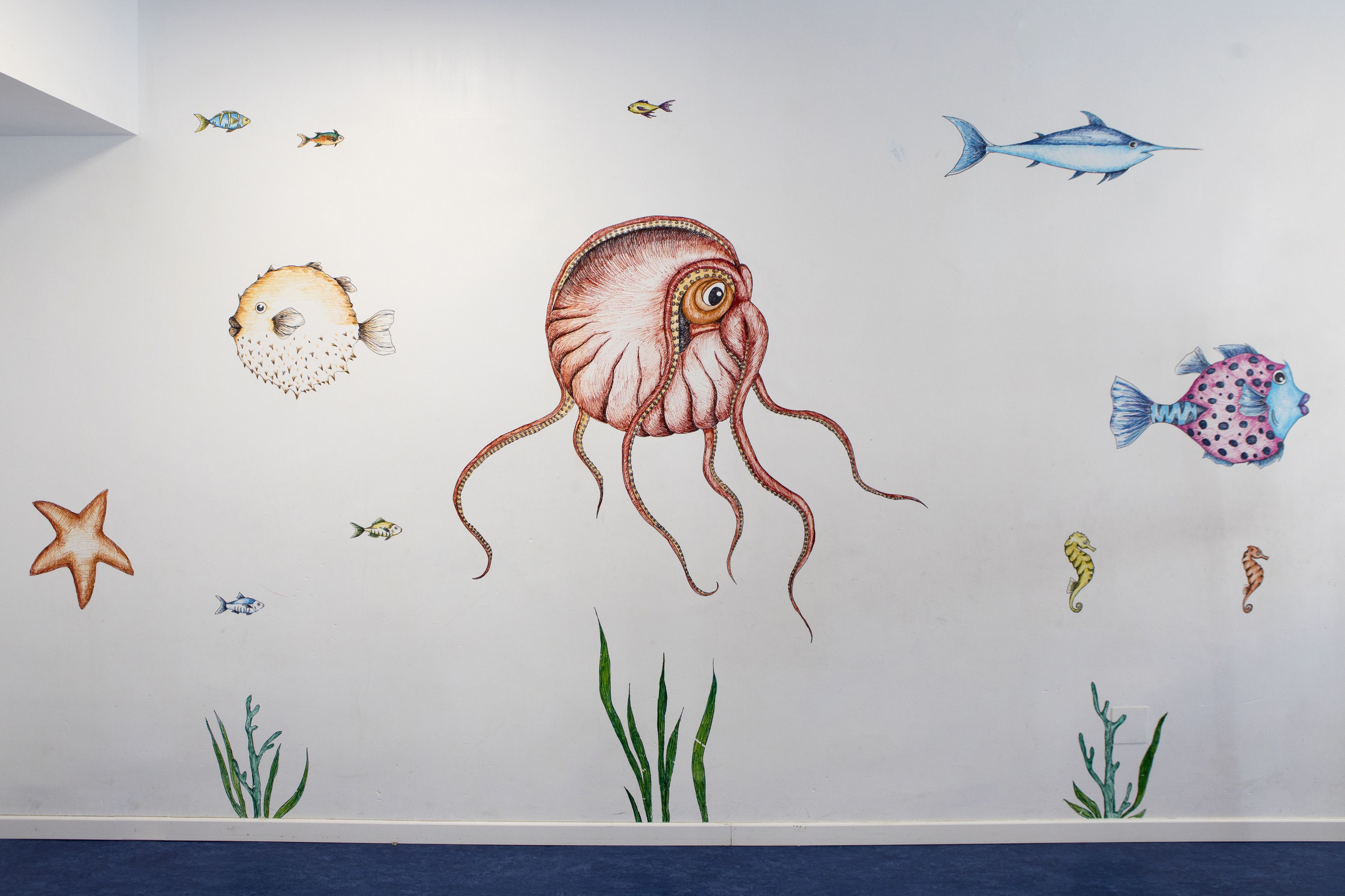 Paret amb diverses criatures marines i plantes, incloent un pou gran, estrelles de mar i peixos.
