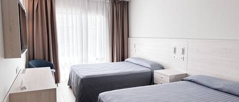 Een moderne hotelkamer met twee bedden, een bureau, een stoel en een groot raam met gordijnen.