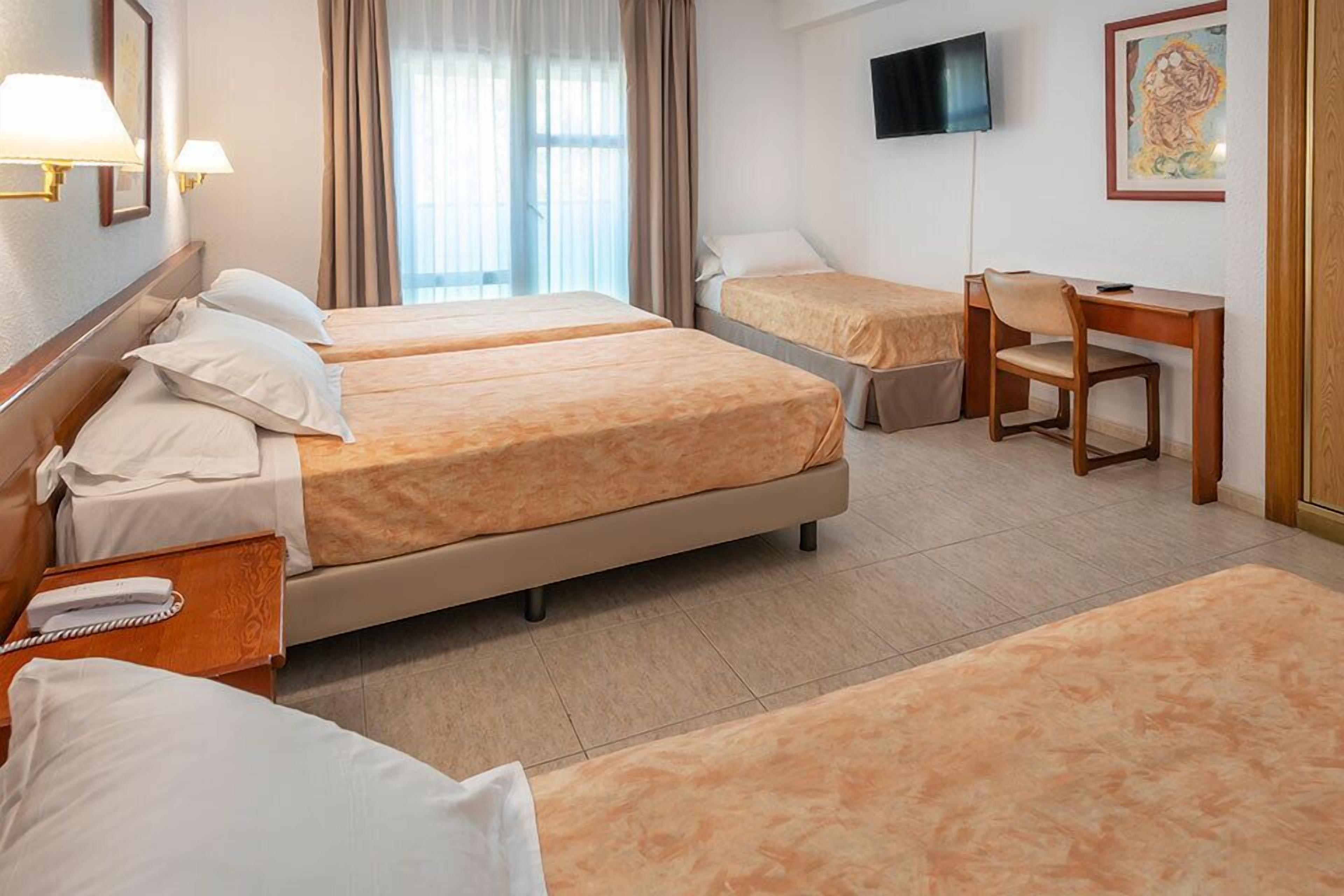 A hotel room with two beds, a desk, a chair, and a TV on the wall.