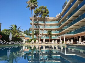 A hotel with a pool, multiple balconies, and outdoor seating areas. - Hotel Canada Palace (Calafell)