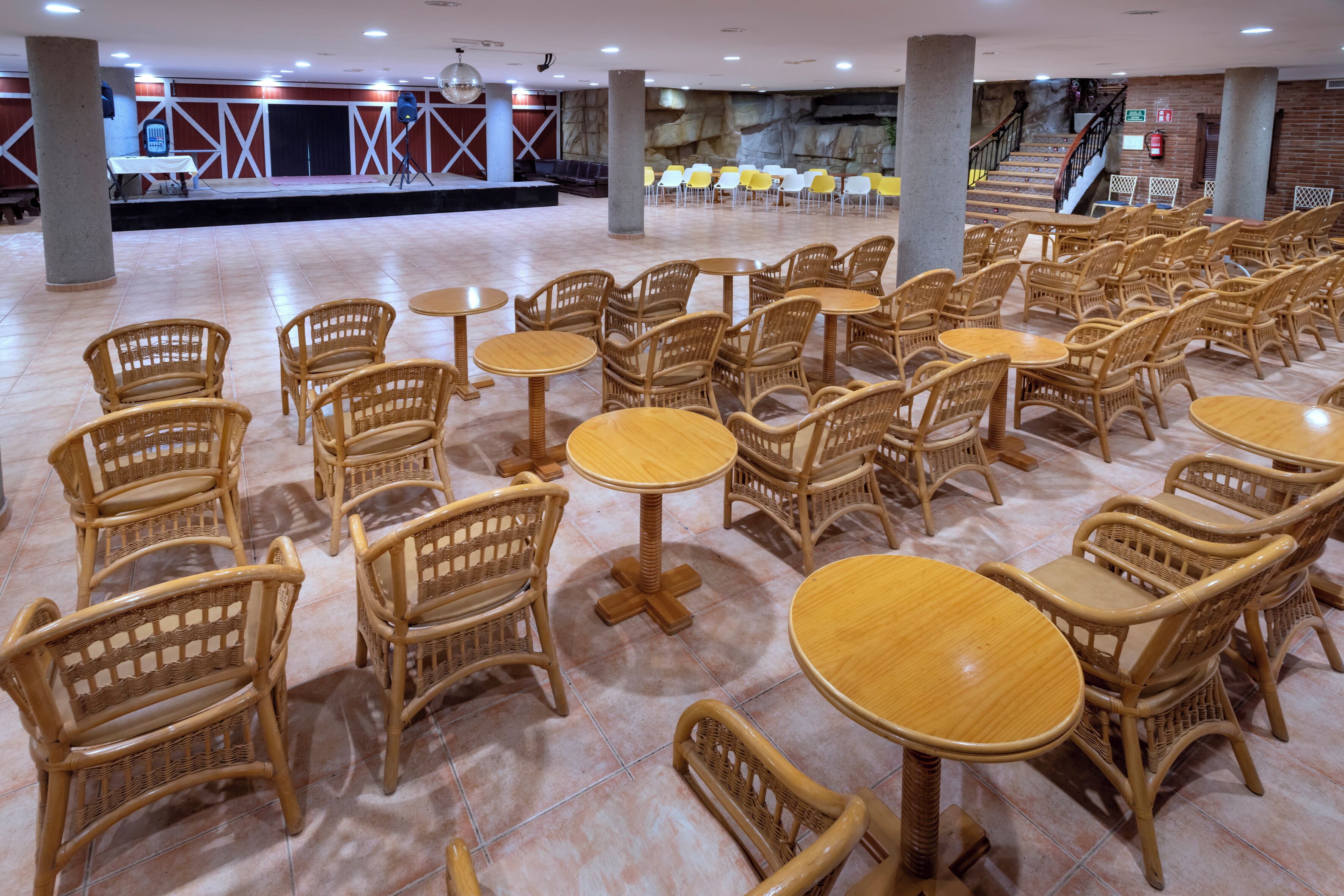 A spacious indoor area with multiple wicker tables and chairs arranged in rows.