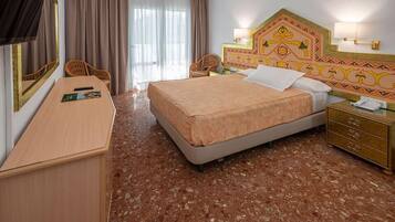 Een hotelkamer met een bed, een bureau, een stoel, een nachtkastje en een spiegel.
