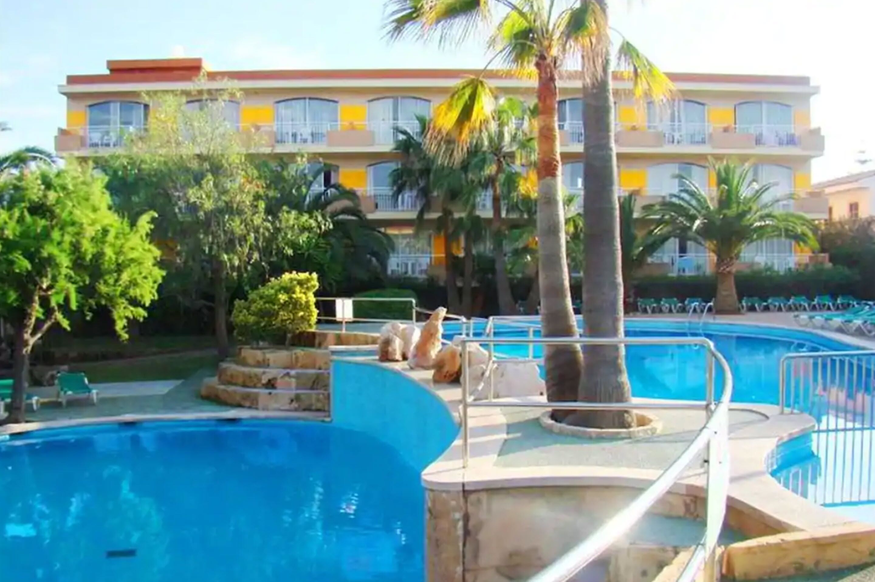 Zona de piscina con palmeras y un edificio al fondo.