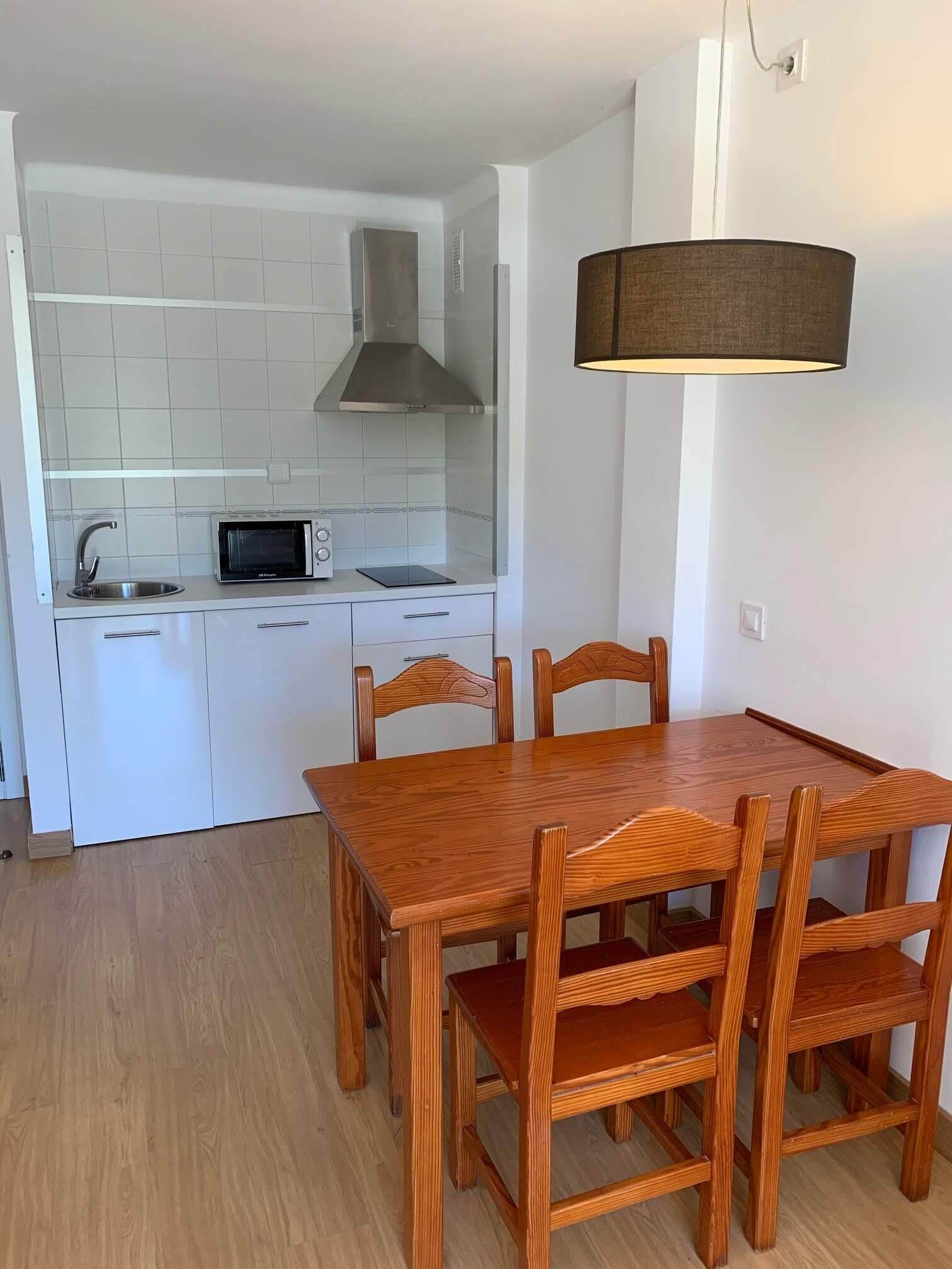 A compact kitchen with white cabinets, a microwave, and a stove. There is a wooden dining table with chairs.