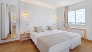 Une chambre d’hôtel avec deux lits, un grand miroir, des lampes de chevet, une fenêtre avec des rideaux et un plancher en bois.