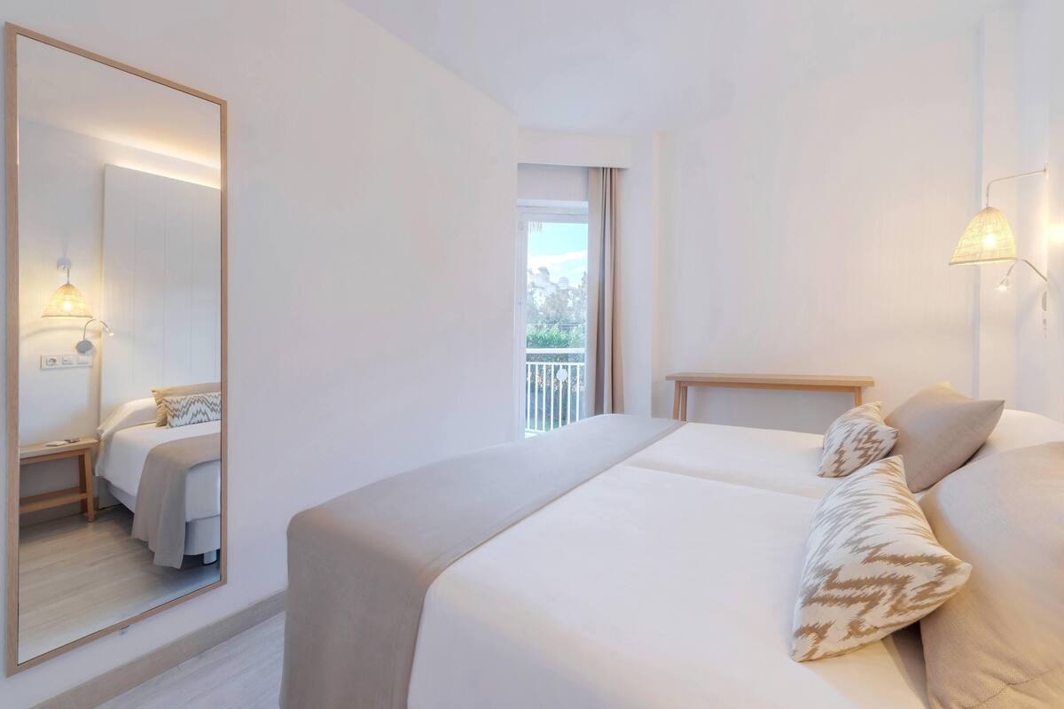 Habitación de hotel con una cama grande, una mesita de noche, un espejo y un balcón con vistas.