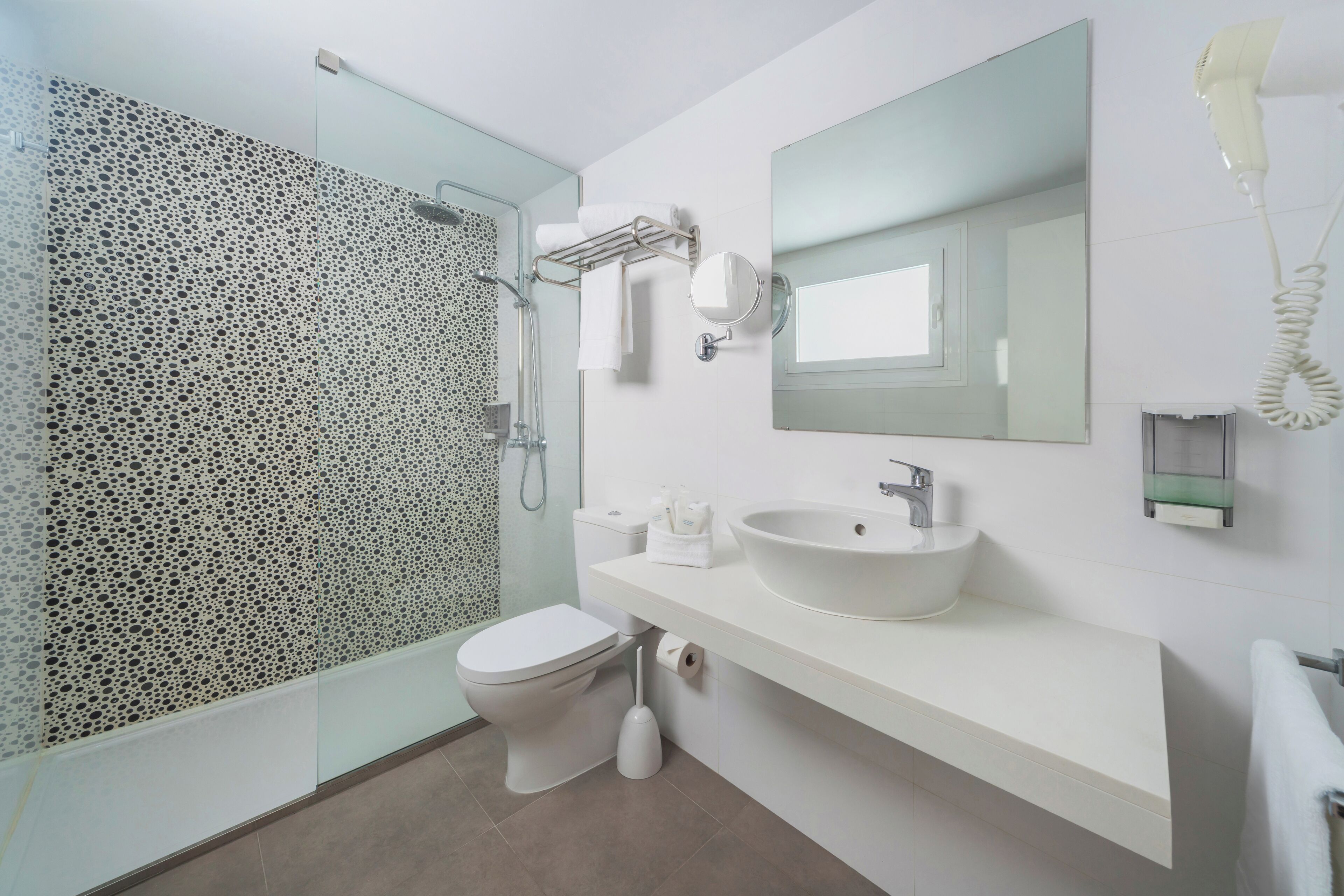 A modern bathroom with a glass shower enclosure, a white sink, a mirror, and a hairdryer.