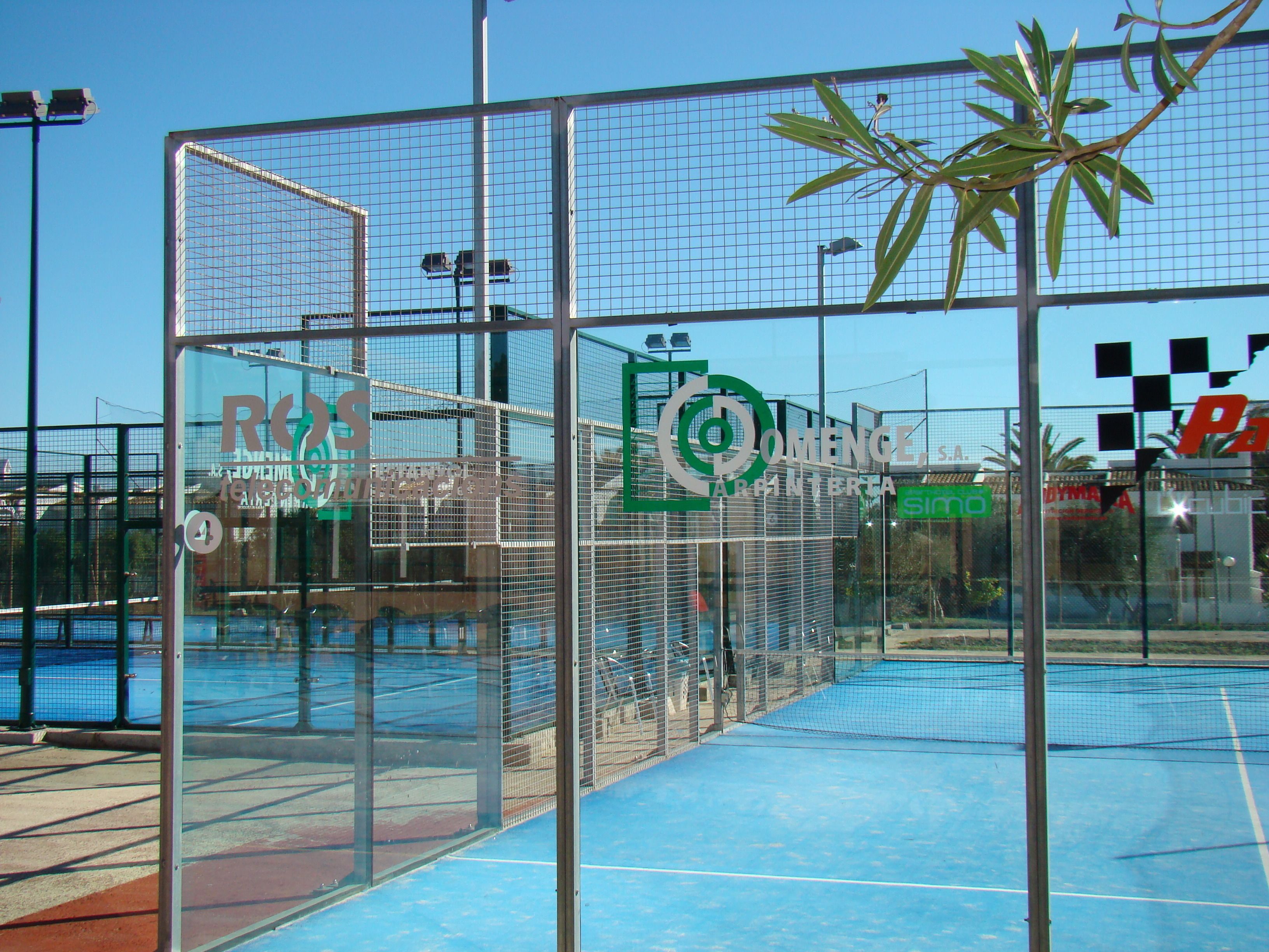 A sports facility with multiple tennis courts, a netted enclosure, and a clear blue sky.
