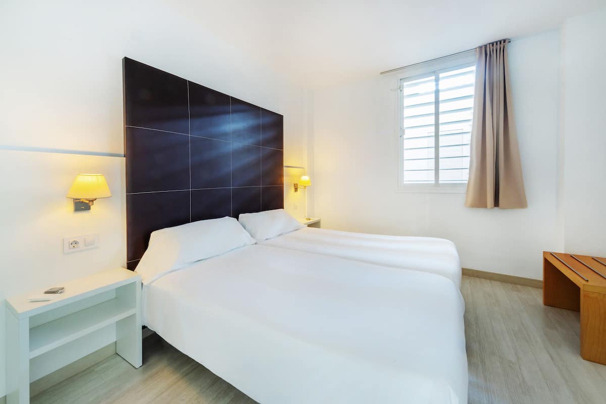 Una habitación de hotel moderna con una cama grande, lámparas de noche, una mesita de noche y una ventana con cortinas.
