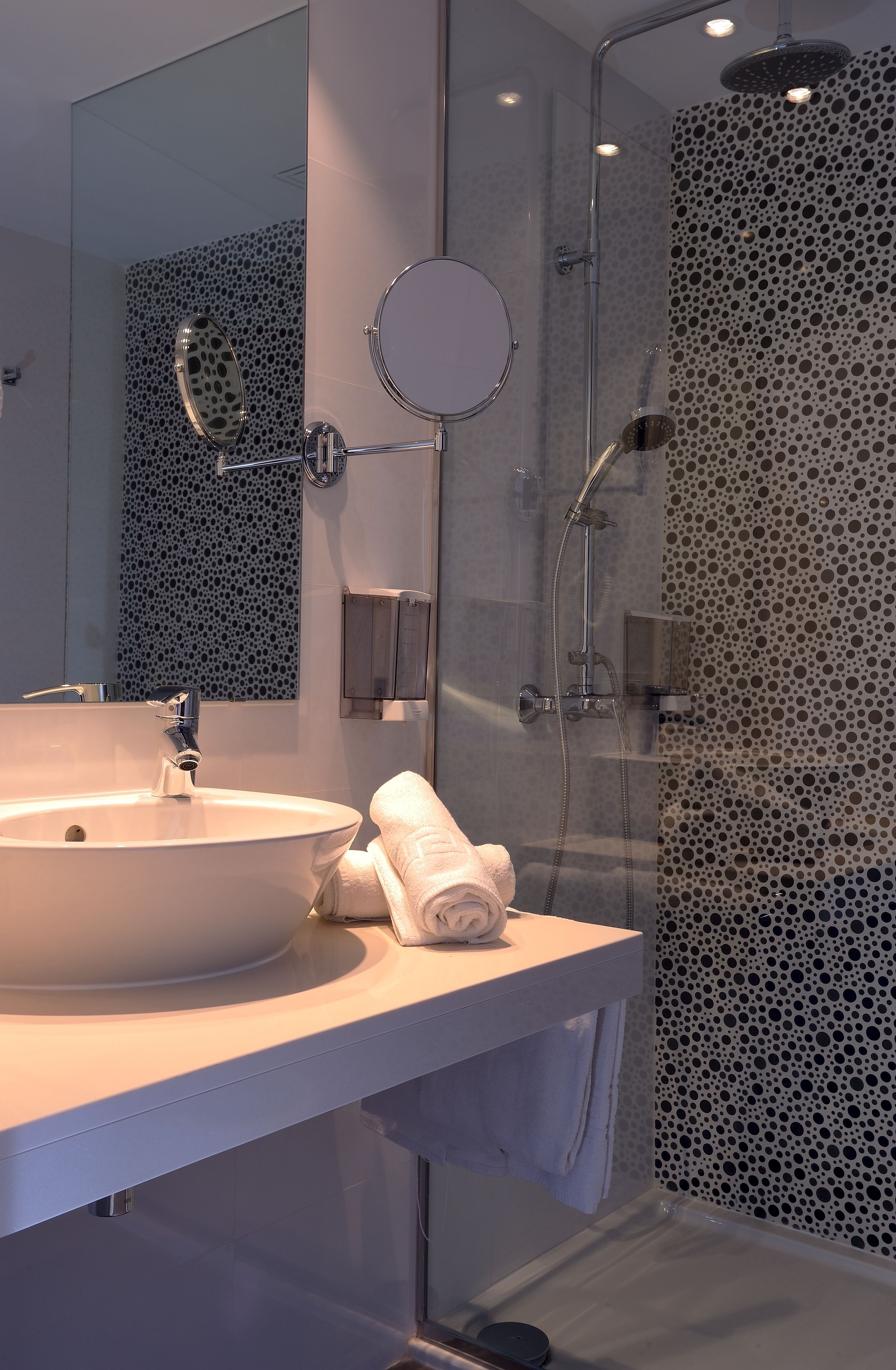 Een moderne badkamer met een groot wastafel, een spiegel, een handdouche en een douchecabine met glazen wanden.