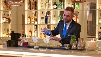 Una zona de bar con un cantinero preparando bebidas, estantes con botellas de licor y lámparas de mimbre colgantes.