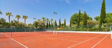 A tennis court with a net, surrounded by trees and a fence.