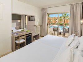 A hotel room with a bed, a desk with a chair, a television, and a view of a pool and buildings.