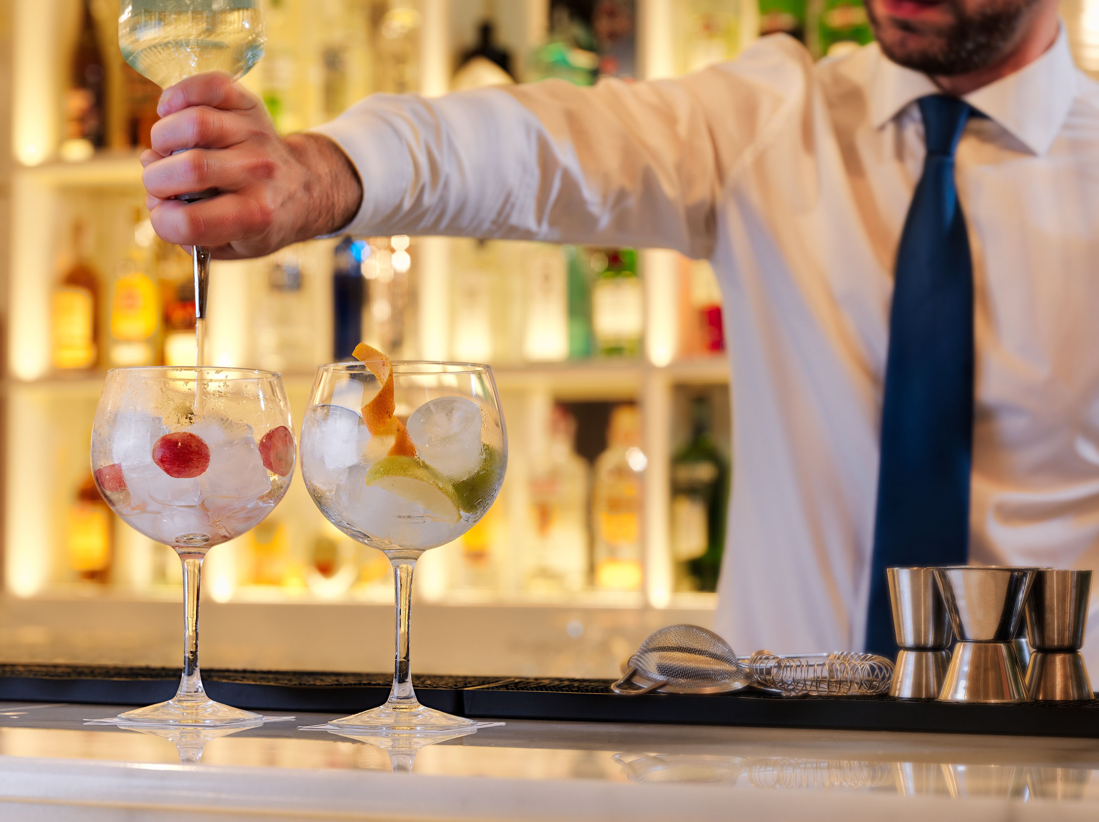 A bartender preparing drinks at a bar with two glasses of cocktail on the counter.