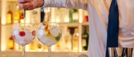 A bartender preparing drinks at a bar with two glasses of cocktail on the counter.