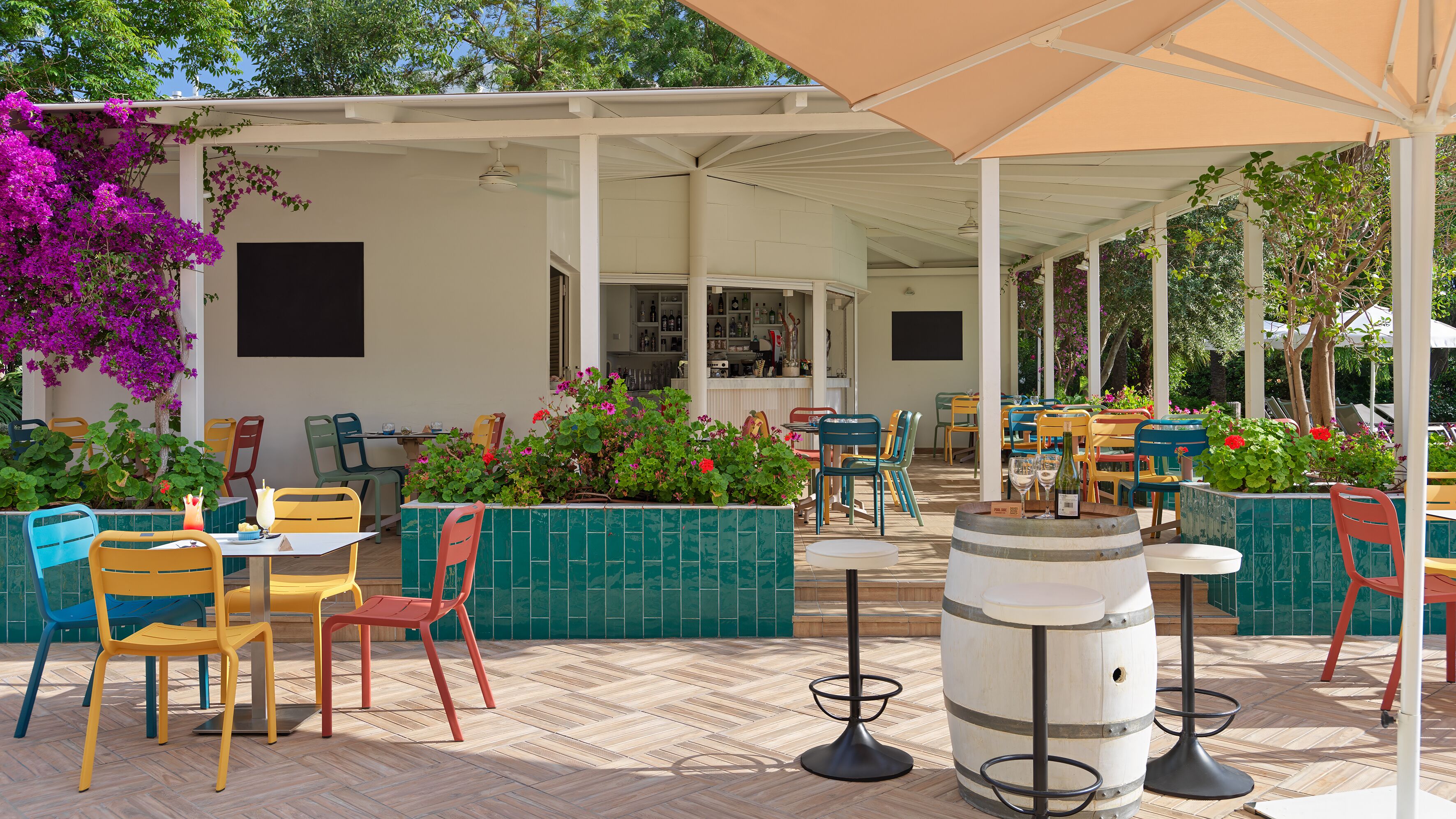 Un patio exterior con sillas y mesas de colores, una zona de bar y plantas en macetas.