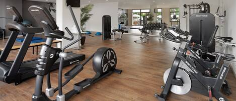Un gimnasio con máquinas de cardio, equipo de levantamiento de pesas y un espejo grande.
