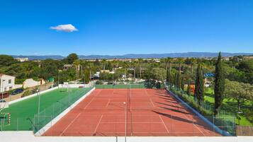 Una cancha de tenis con superficie verde y roja, rodeada de árboles y un cielo despejado.