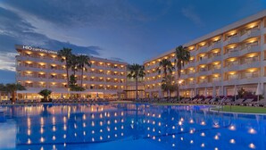 A hotel with multiple balconies, a swimming pool, and palm trees. - H10 Cambrils Playa (Cambrils)