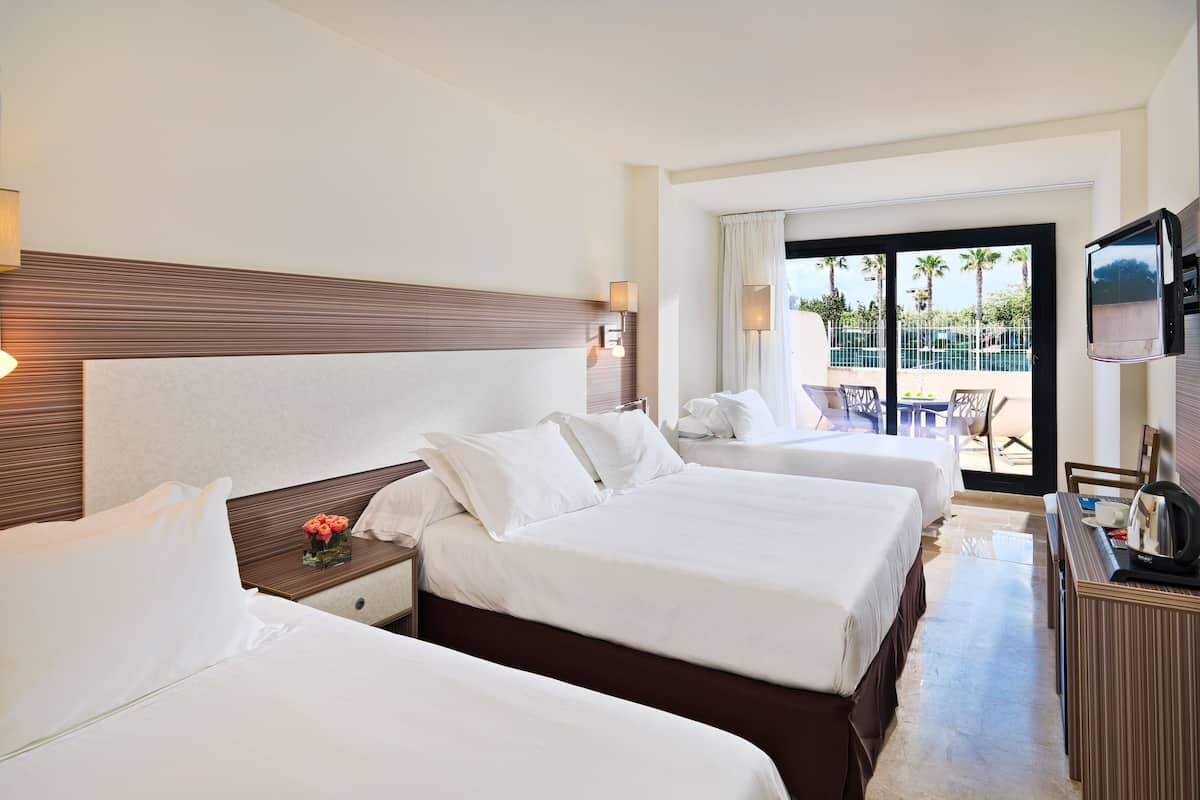 A hotel room with two beds, a TV, and a balcony with a view of palm trees.