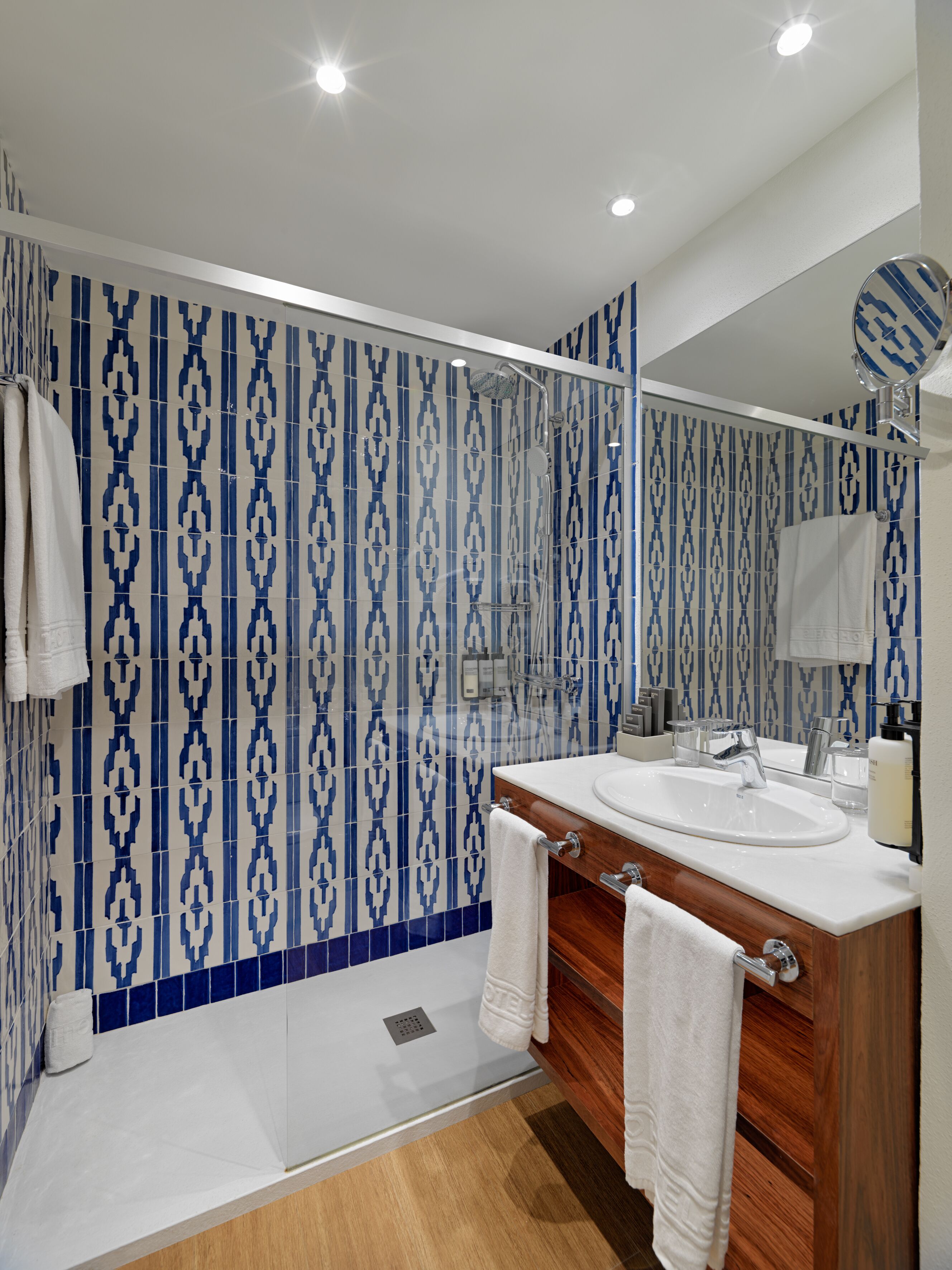 Un baño moderno con un salpicadero de azulejos estampados, una ducha a ras de suelo y un tocador con espejo.