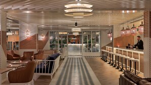 A modern hotel lobby with a central staircase, a reception desk, and a bar area with stools. - H10 Cambrils Playa (Cambrils)