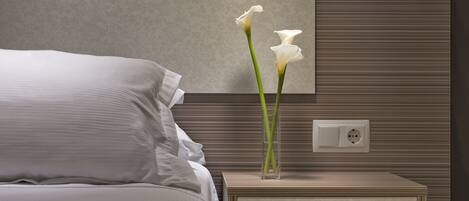 Une chambre à coucher moderne avec un lit, une table de chevet ornée d’un vase de fleurs et un luminaire fixé au mur.