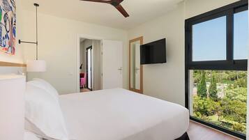 A bedroom with a bed, a ceiling fan, a TV, and a large window with a view.