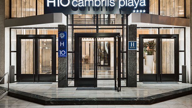The entrance to H10 Cambrils Playa hotel with a modern design, featuring a prominent sign and a glass door entrance. - H10 Cambrils Playa (Cambrils)
