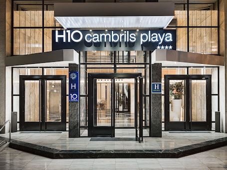 The entrance to H10 Cambrils Playa hotel with a modern design, featuring a prominent sign and a glass door entrance.