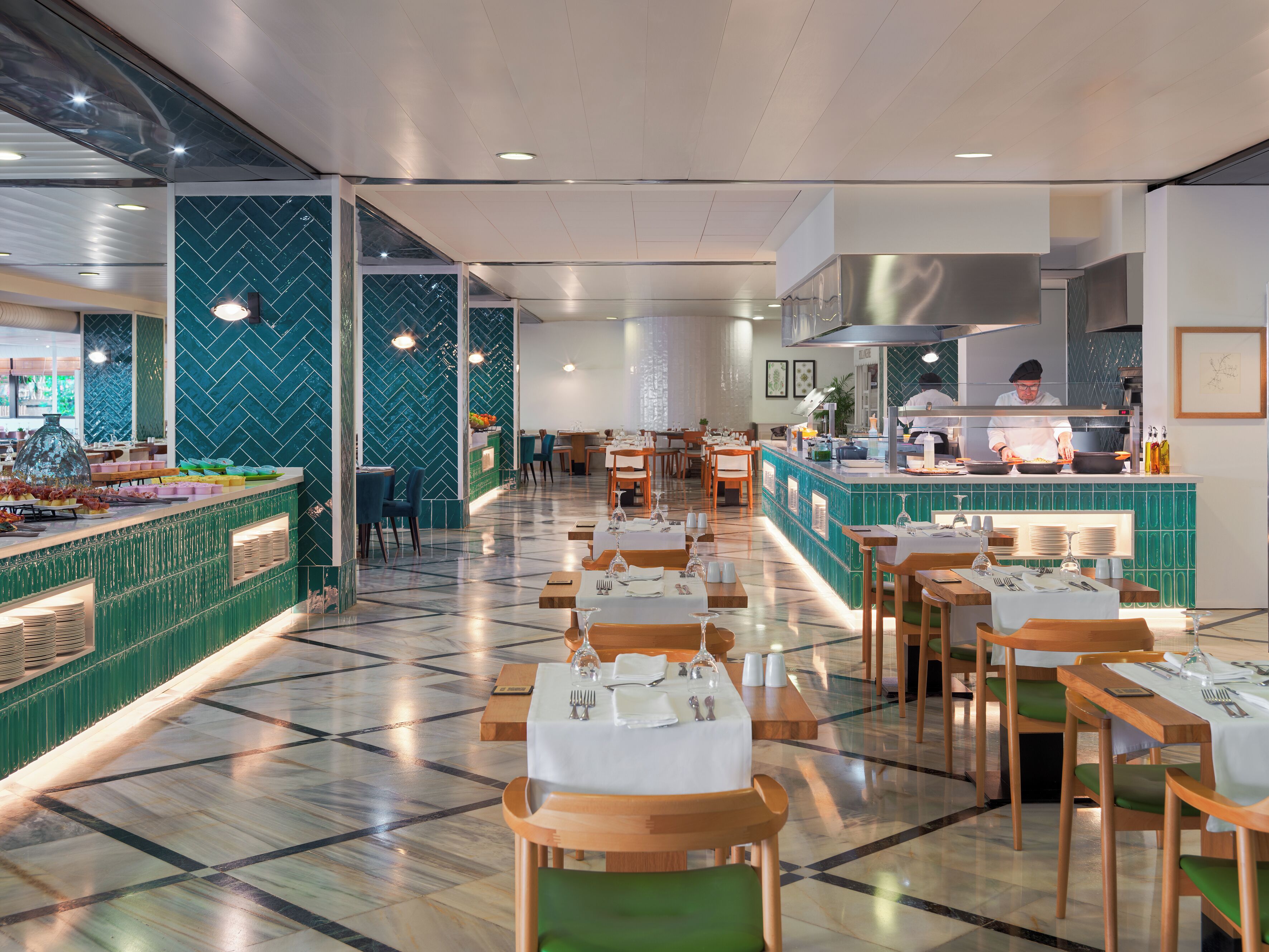 Un restaurante moderno con una barra alargada, varias mesas y una zona de cocina central.