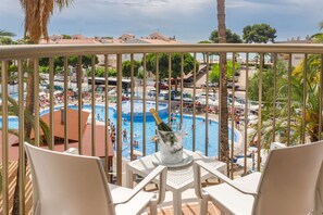 A balcony with white chairs, a pool area with people, and a bottle of champagne in a bucket. - Hotel Best Cambrils (Cambrils)