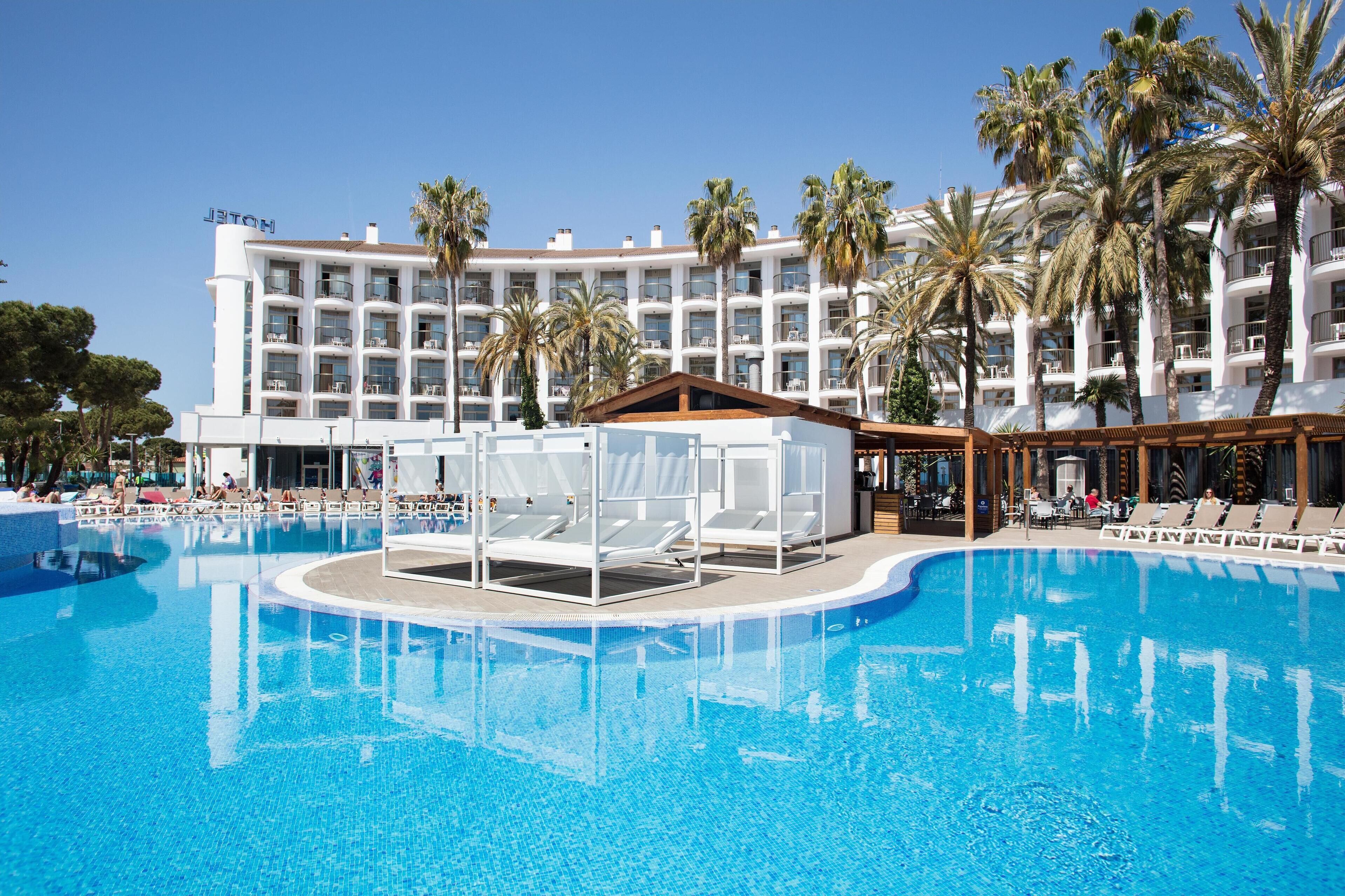 A hotel with a large pool, palm trees, and a clear blue sky.