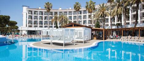 A hotel with a large pool, palm trees, and a clear blue sky.