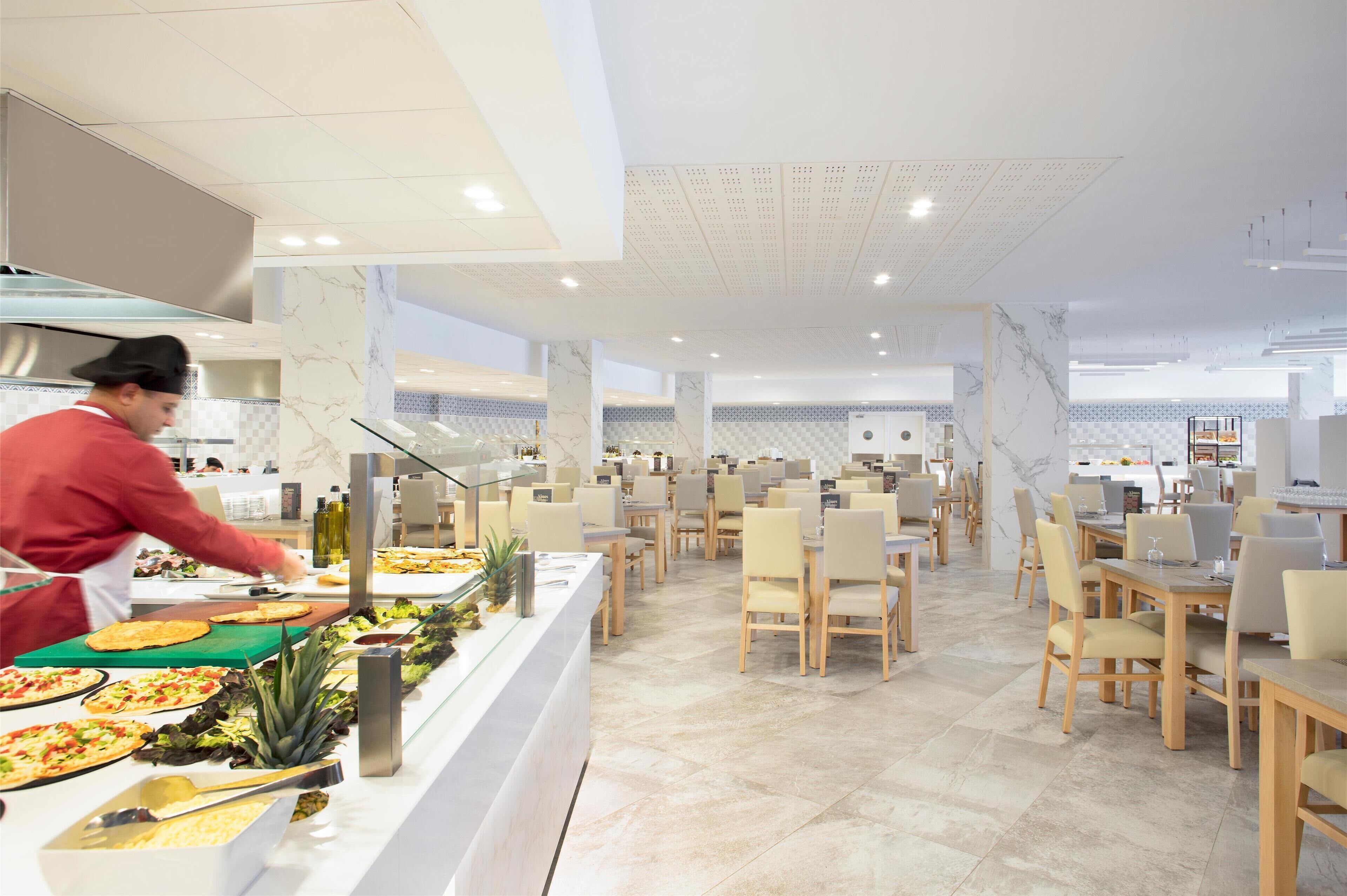 Une cafétéria moderne avec un chef qui prépare les plats, des murs en marbre et un aménagement propre et spacieux.