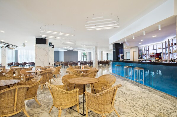 A spacious indoor area with wicker tables and chairs, a bar area with a blue countertop, and a large window providing natural light. - Hotel Best Cambrils (Cambrils)