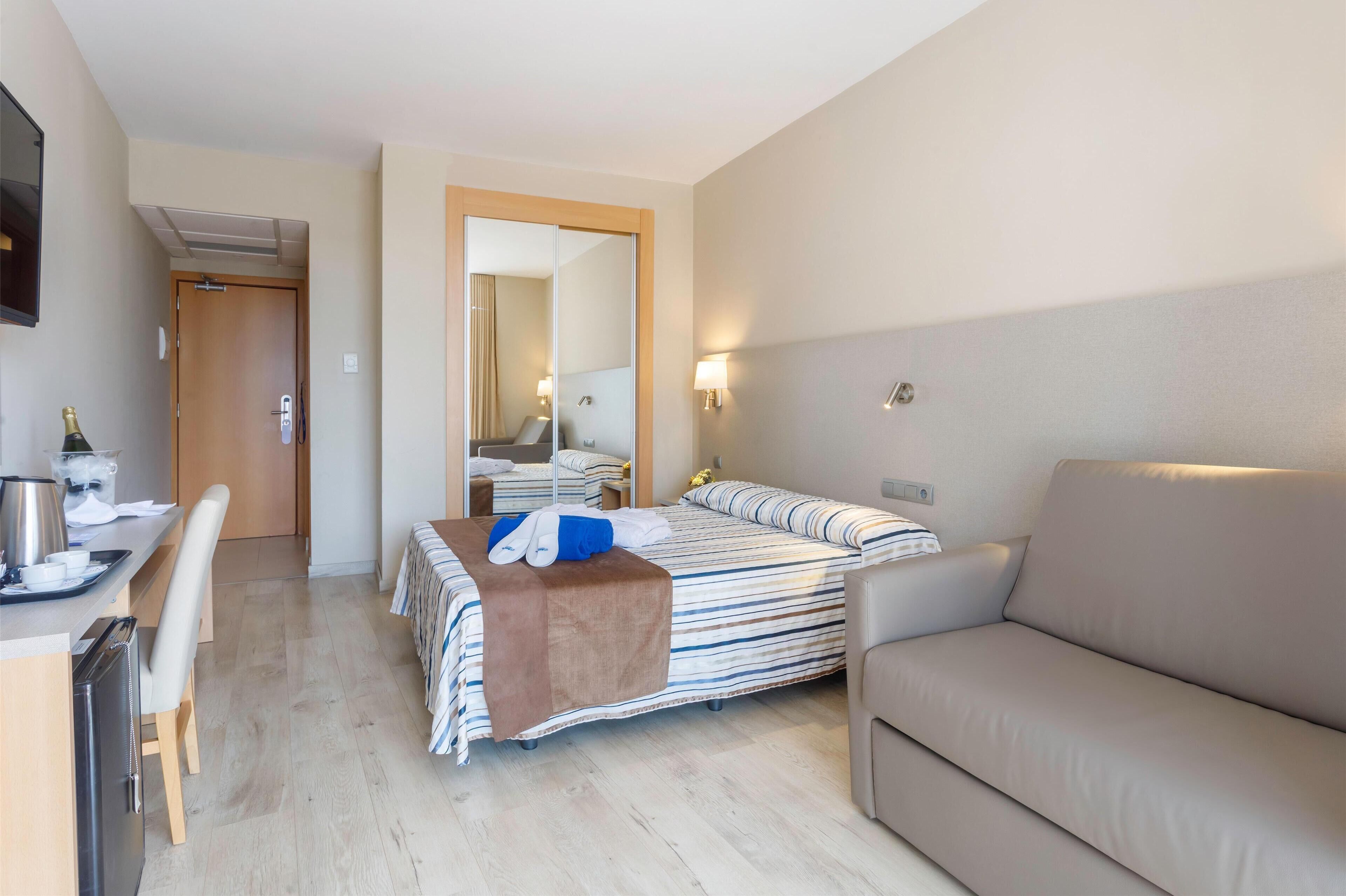 Ein Hotelzimmer mit einem Bett, einer Sitzecke, einem Schreibtisch mit Wasserkocher und einem Spiegel.