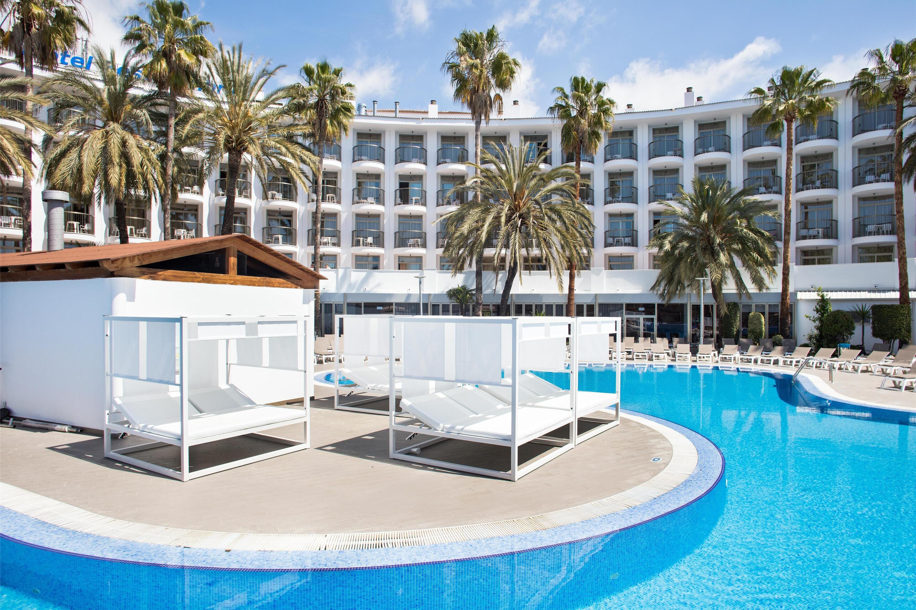 A hotel pool area with sun loungers and palm trees.