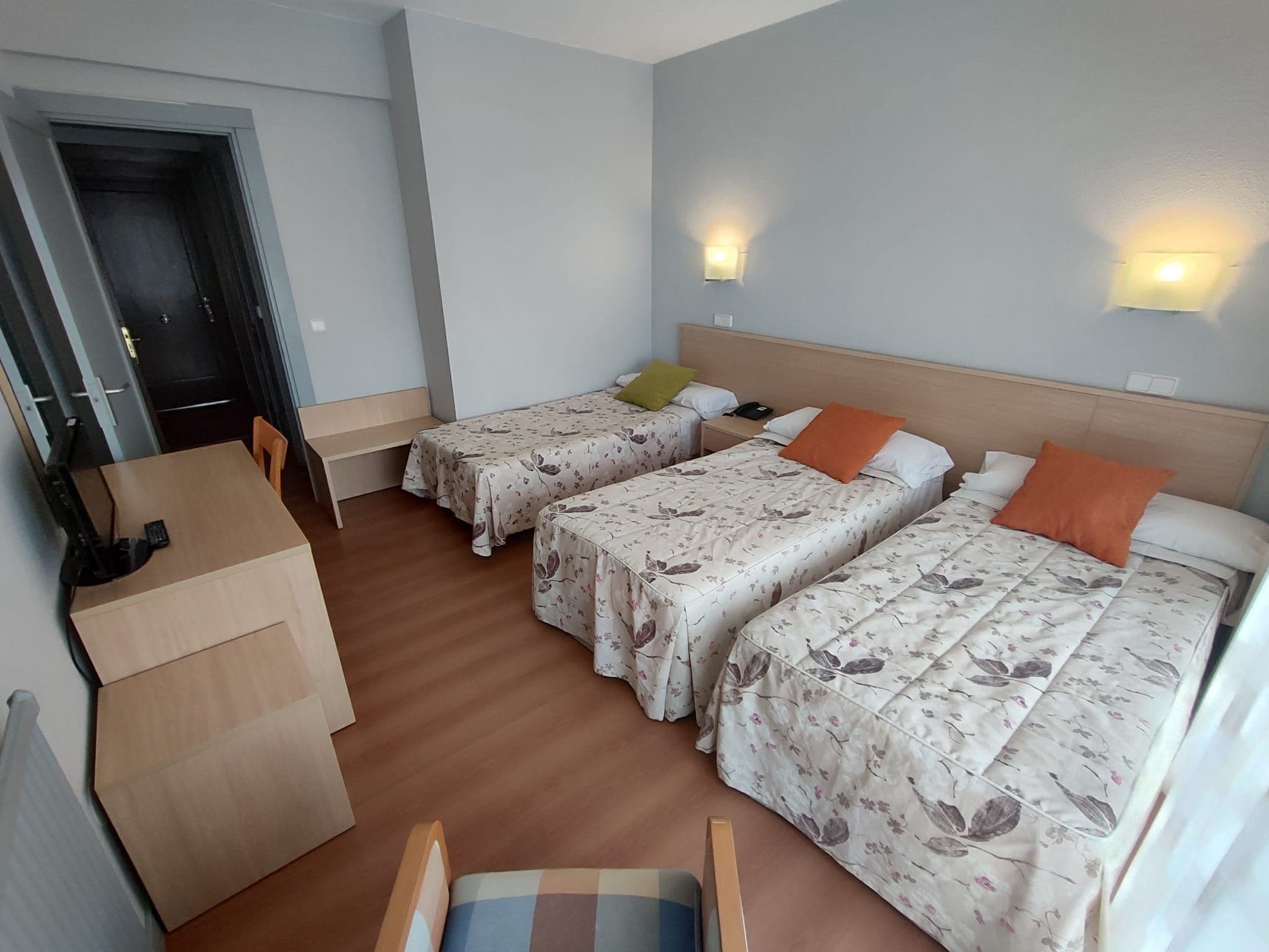 Una habitación de hotel con dos camas, un escritorio, una silla y una puerta.