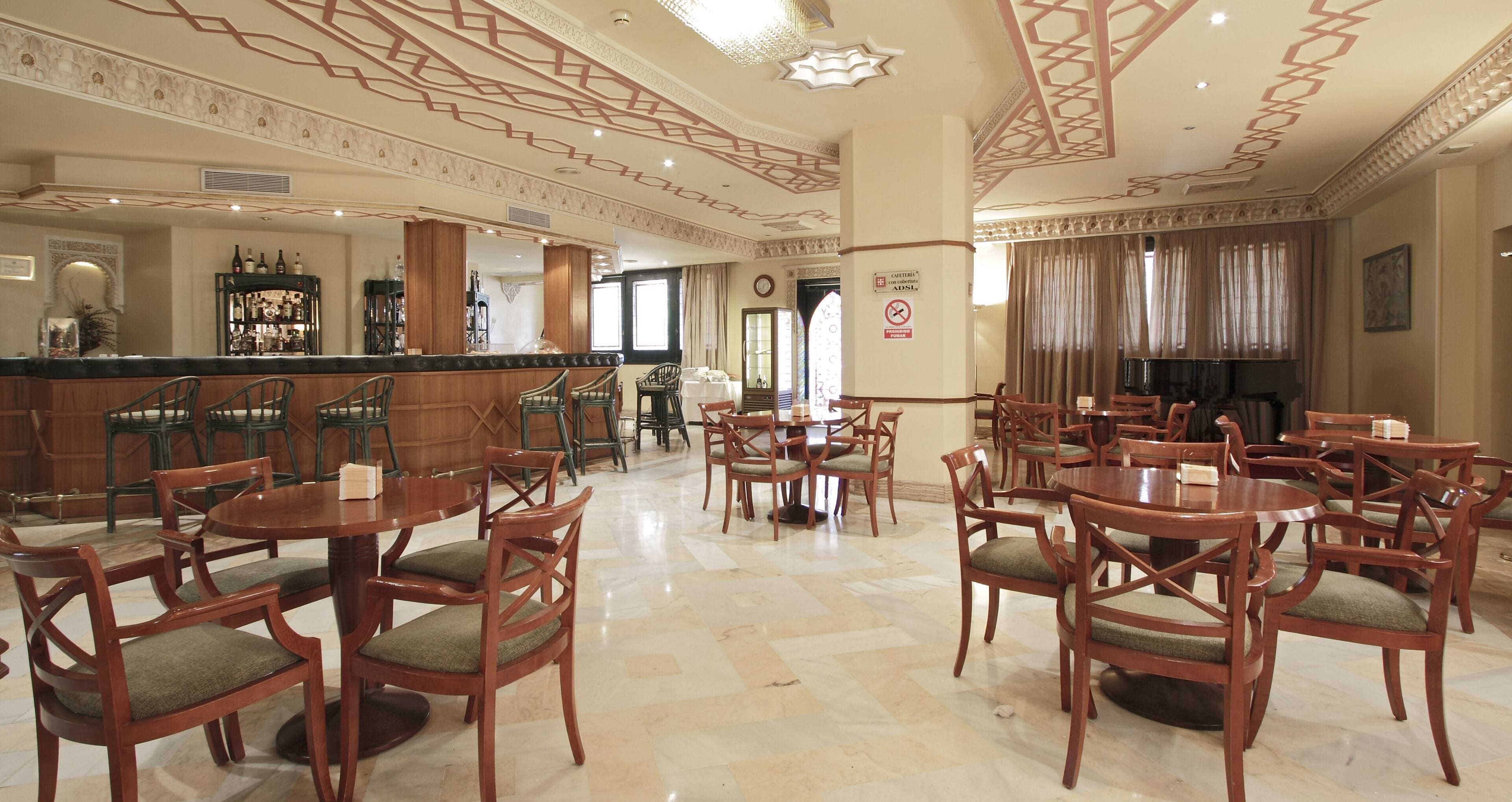 A spacious lobby with multiple wooden tables and chairs, a bar area with bottles, and a decorative ceiling.