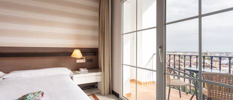 A hotel room with a large sliding glass door leading to a balcony with a city view.