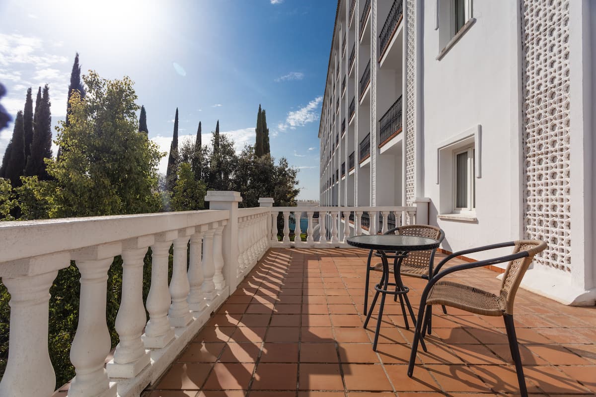 A terrace with a white balustrade, a table with chairs, and a view of trees and a building.
