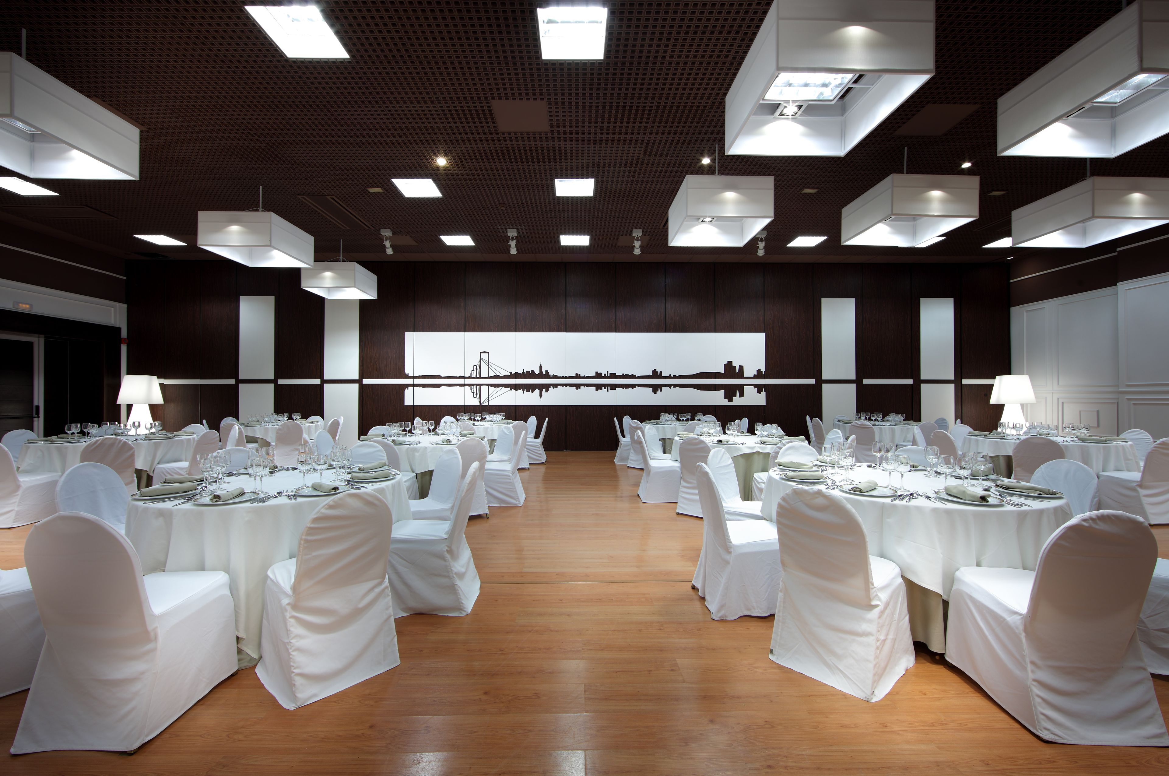 A banquet hall with round tables, white chairs, and a cityscape view.