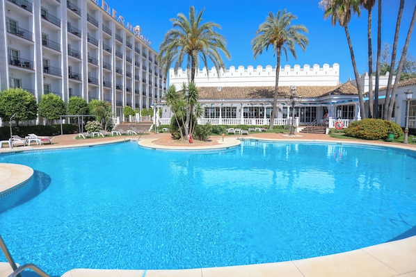 A hotel with a large pool, palm trees, and a building with balconies. - Hotel Abades Benacazón (Benacazon)