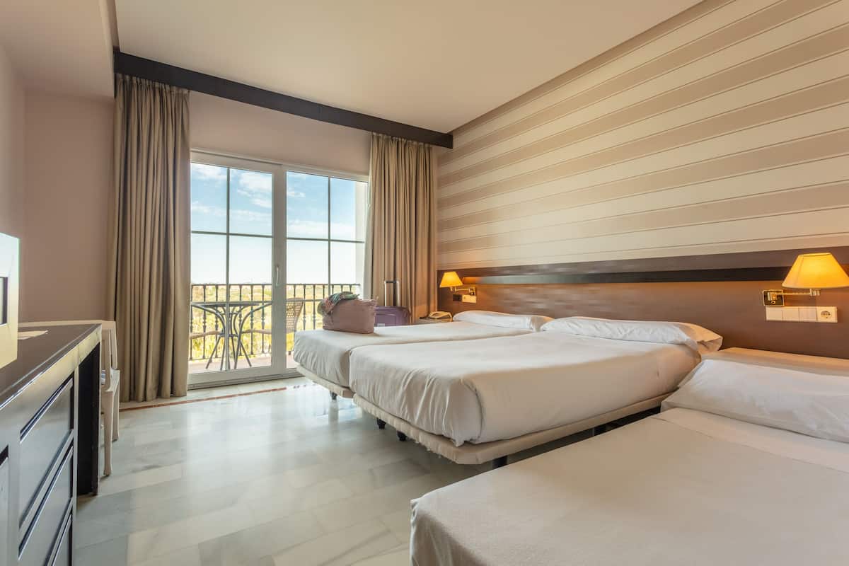 A hotel room with two beds, a desk, a chair, and a balcony with a view.