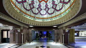 Un vestíbulo imponente con suelo estampado con motivos de estrellas, un techo de vitrales y una zona de recepción moderna.