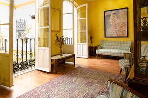 Una habitación con suelo de madera, un sofá a cuadros, un tapiz estampado y un cuadro en la pared.