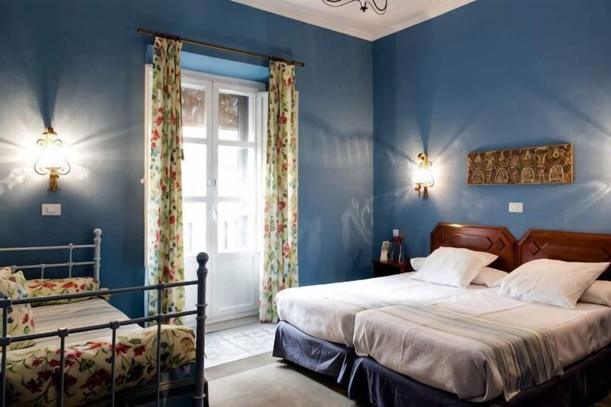 Un dormitorio con cama, mesita de noche, lámpara y ventana con cortinas.